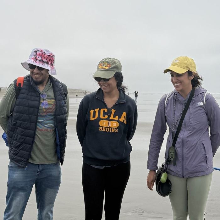 Three community members standing together on a sandy beach